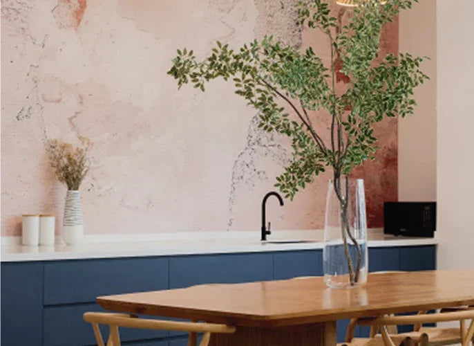 Modern kitchen interior with pink textured wallpaper, blue cabinetry, and a wooden dining table.