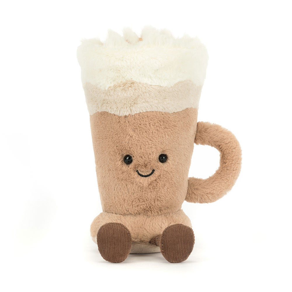 A front view of a plush toy shaped like a latte in a mug, with a fluffy white foam top, tan body, smiling face with black button eyes, a soft handle on the side, and brown corduroy feet, sitting upright and looking cheerful.