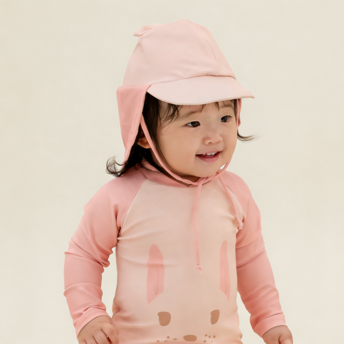 Baby wearing Le Petit Society Baby Bunny Sunhat and matching pink bunny rash guard swimsuit