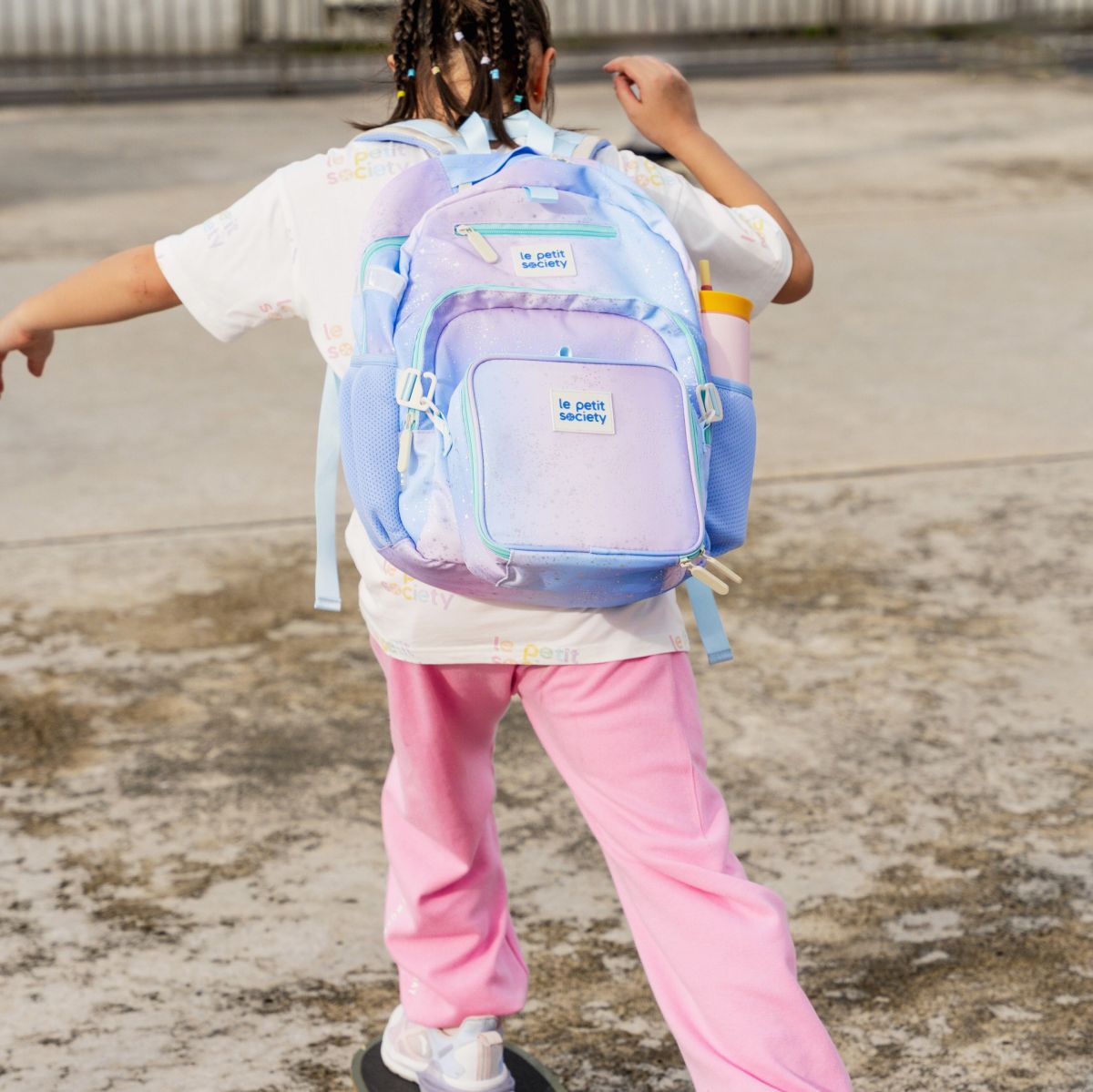 A primary school girl carrying a single pocket school bag in a purple galaxy print.