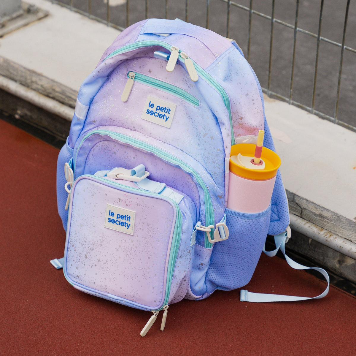 A purple and blue ombre kids school bag with a thermal lunch bag attached at the front.