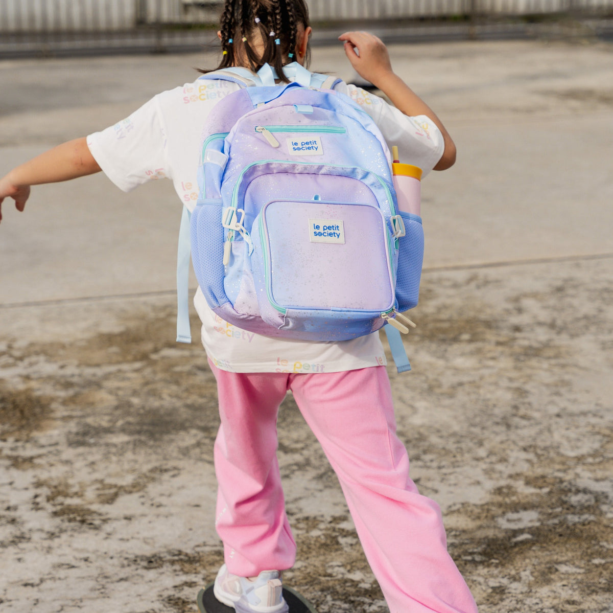 A primary school girl carrying a single pocket school bag in an ombre purple and blue design.