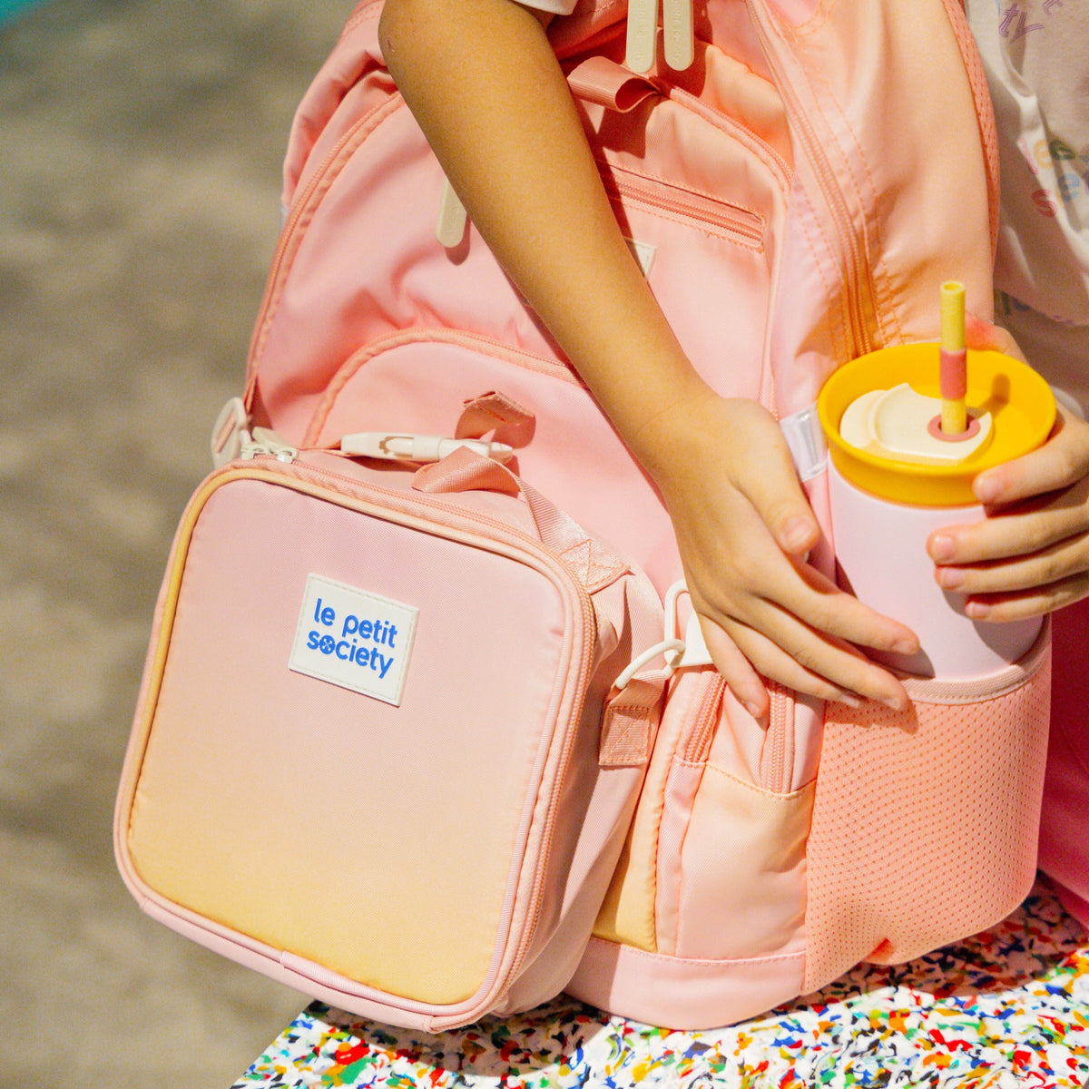 A kid storing her water bottle in the sleeve of her LPS kids double pocket backpack.