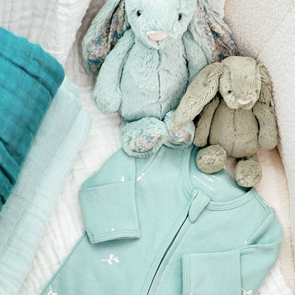 Two bunny plush toys from Jellycat next to a mint blue organic baby zip sleepsuit from Le Petit Society.