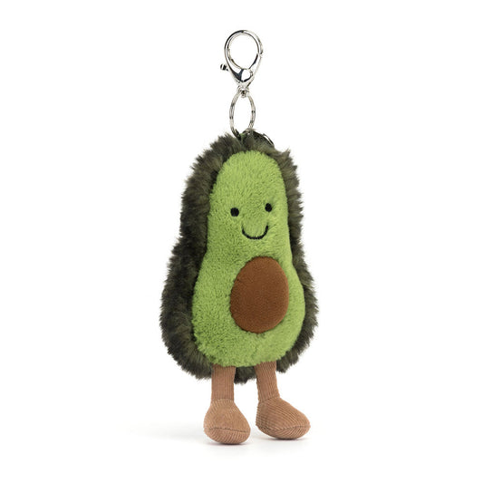 A front view of a soft plush keychain shaped like a smiling avocado half with a brown seed, black bead eyes, green fuzzy outer skin, and brown corduroy legs.