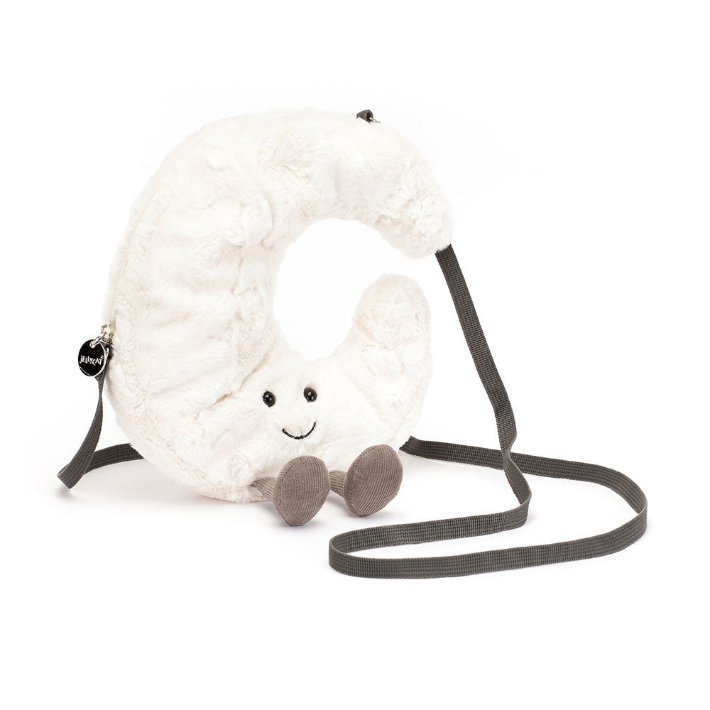 A front view of a soft plush crescent moon-shaped crossbody bag with a smiling face, black bead eyes, brown corduroy legs, and a long dark gray strap.