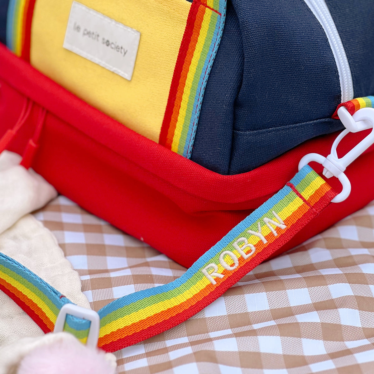 A close-up of a personalised name embroidery on a rainbow bag strap from Le Petit Society.