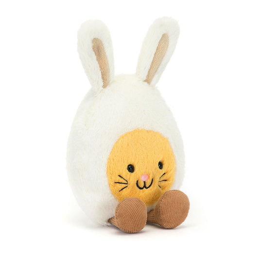 A front view of a egg shaped soft plush toy with bunny ears and a yellow face with whiskers. It has black button eyes, a pink embroidered nose, a happy smile, and brown corduroy feet