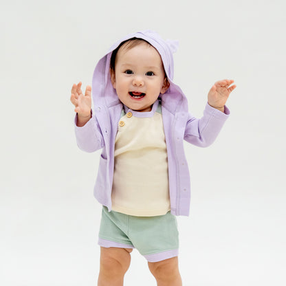 A baby boy wearing a coordinating set of a colour block tee and boxers, complete with a lilac purple bunny cardigan from Le Petit Society.
