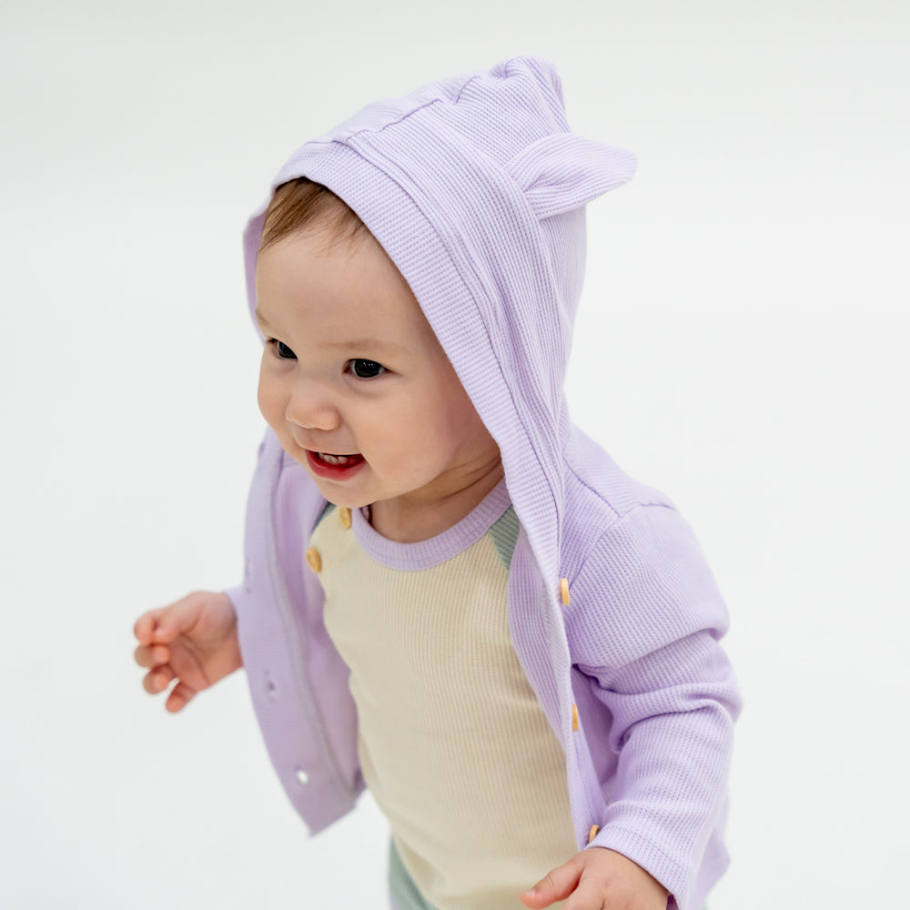 A baby boy wearing a coordinating set of a colour block tee and boxers, complete with a lilac purple bunny cardigan from Le Petit Society.