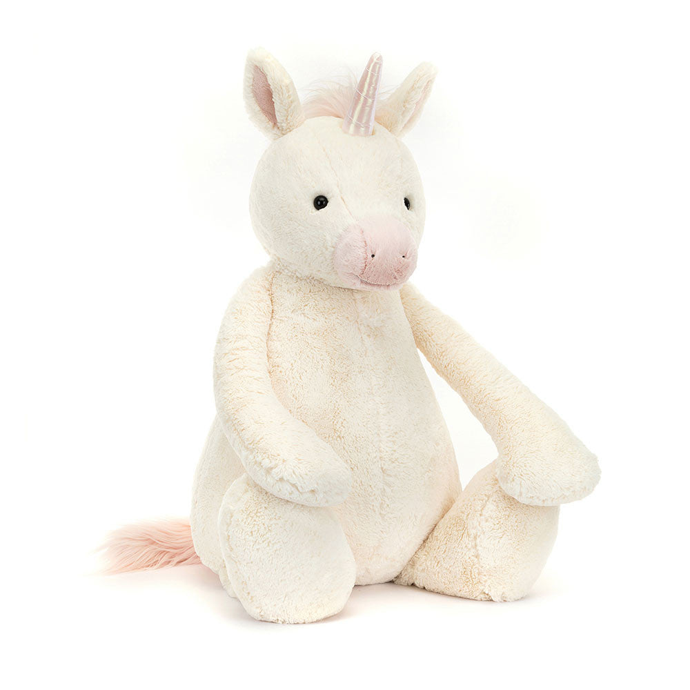 A front view of a soft cream-colored giant plush unicorn toy with a pink snout, fluffy pink mane and tail, shiny iridescent horn, and black embroidered eyes, sitting upright.