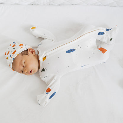 A newborn baby wearing a white, organic zip sleepsuit with foldable mittens and footies by Le Petit Society, featuring a forest motif with brown bears.