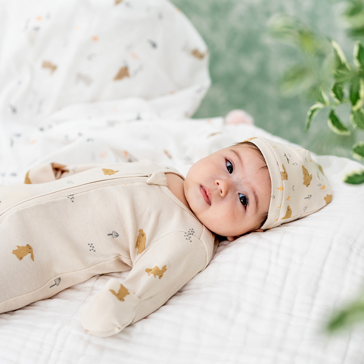 A baby wearing an organic zip sleepsuit with foldable mittens and footies by Le Petit Society, featuring a woodland-themed motif with rabbits over a beige base. 