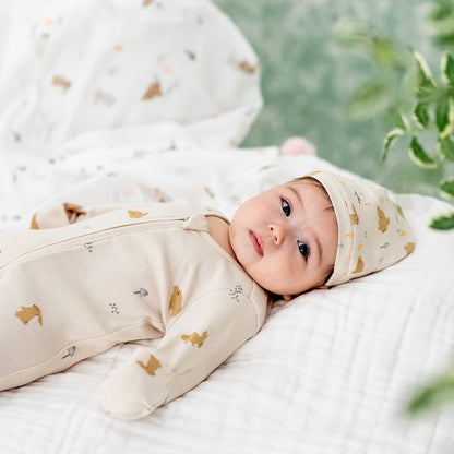 A baby wearing an organic zip sleepsuit with foldable mittens and footies by Le Petit Society, featuring a woodland-themed motif with rabbits over a beige base. 