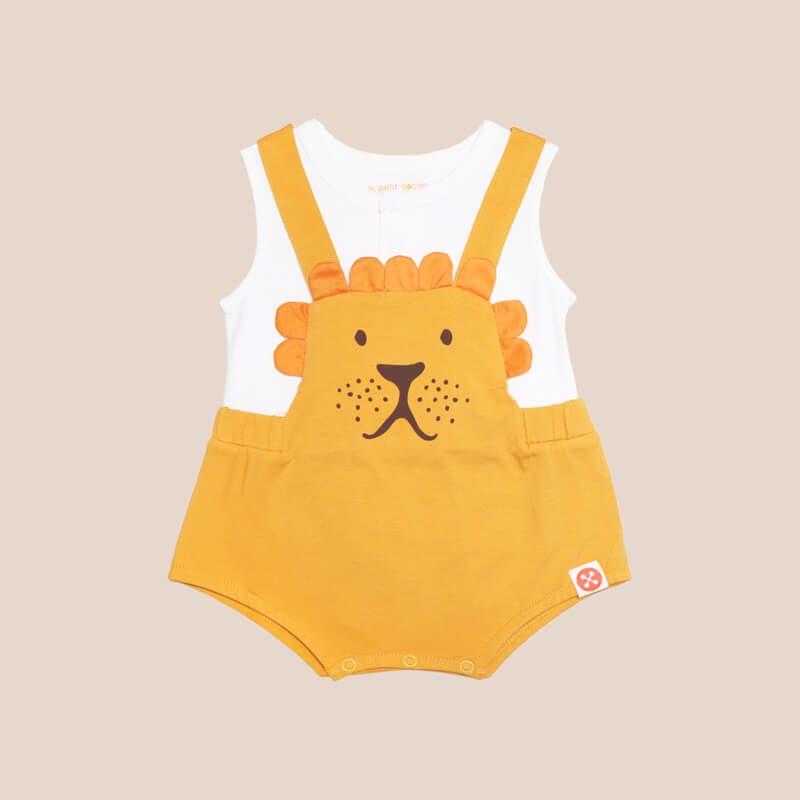 An animal-themed baby romper by Le Petit Society, featuring a lion's face at the front, complete with bottoms and cross back straps in yellow-orange over a white undershirt.