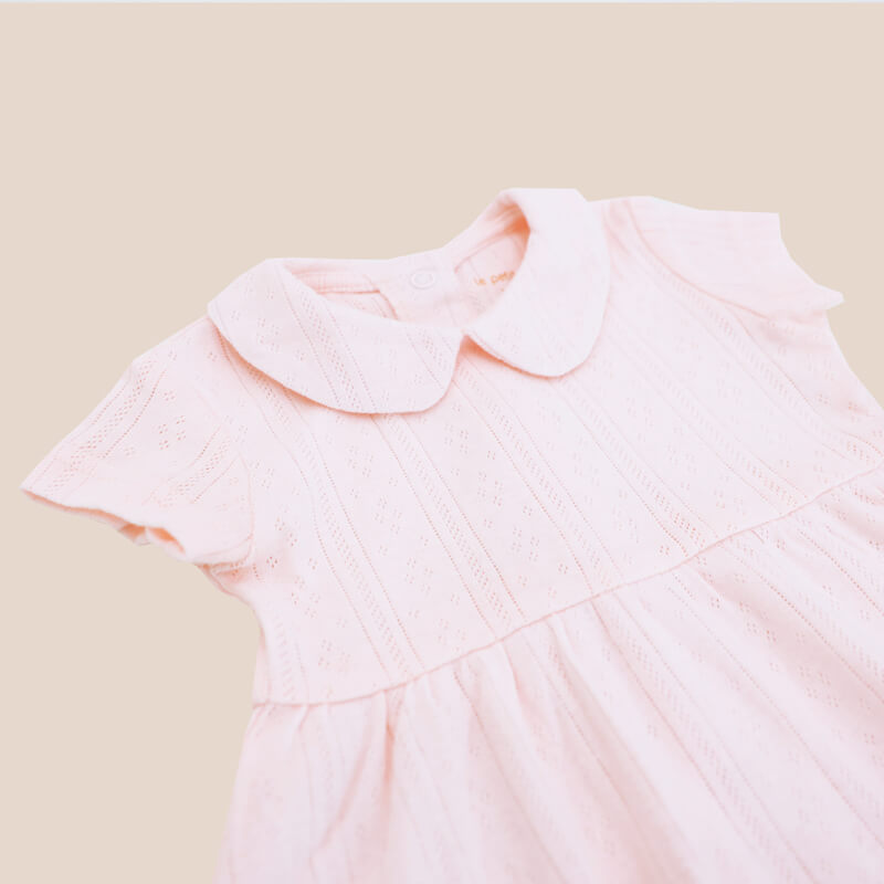 A close-up of a baby girl dress from Le Petit Society. It comes with a peter pan collar and is made in a pink pointelle cotton.
