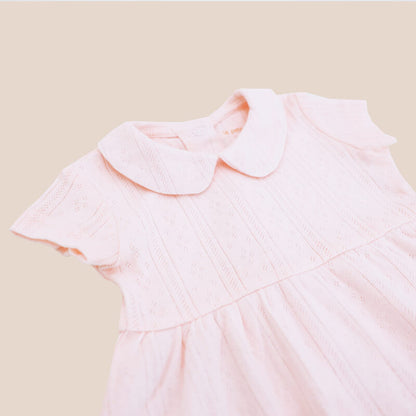 A close-up of a baby girl dress from Le Petit Society. It comes with a peter pan collar and is made in a pink pointelle cotton.
