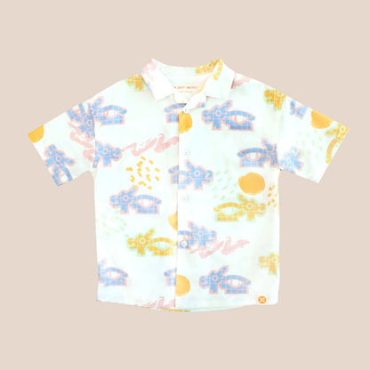 White short-sleeve boys’ button-up shirt from Le Petit Society with camp collar in colorful dragon playground print and sun print in pastel blue, yellow, green, and pink.