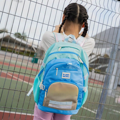 A primary school girl carrying the double pocket school bag in blue and iridescent silver.