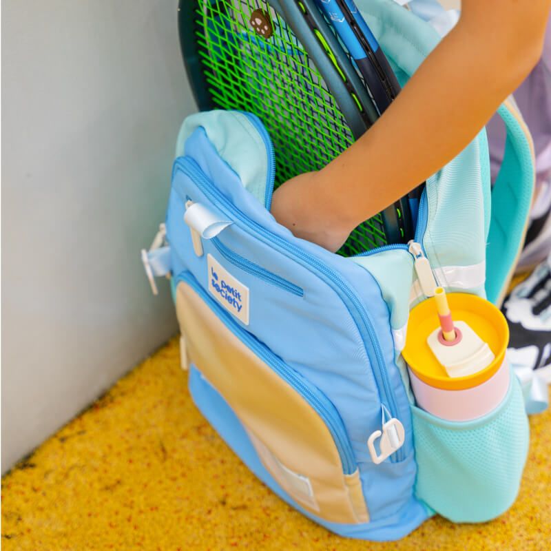A sports racket being kept in a double pocket school bag.