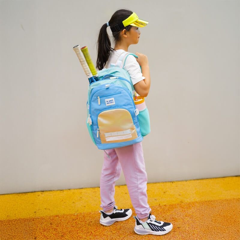 An athletic girl carrying the double pocket school bag with sports rackets sticking out of her bag.