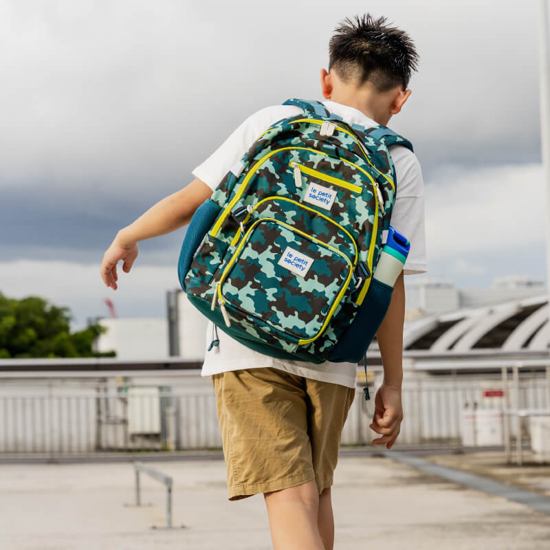 A primary school boy carrying the LPS kids double pocket school bag in a green camouflage print.