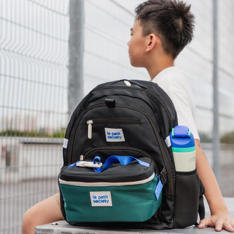A primary school boy with his double pocket school bag in black and green.