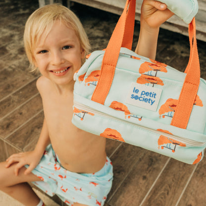A primary school boy carrying a mint-coloured thermal lunch bag with a croissant print and orange strap from Le Petit Society.