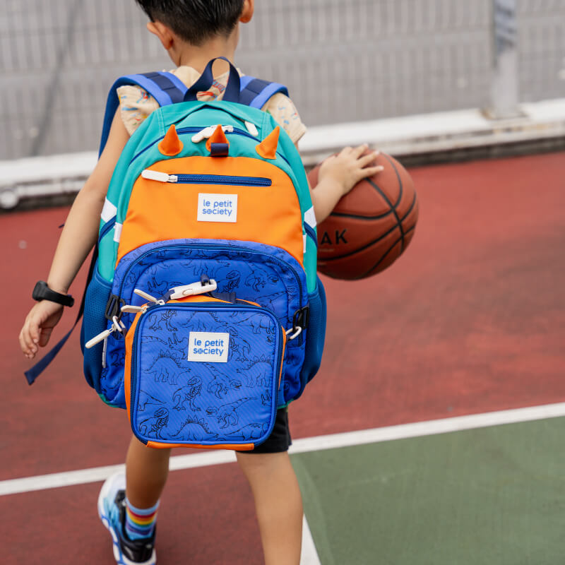 A sporty primary school playing basketball with his LPS kids single pocket school bag in dinosaur print.