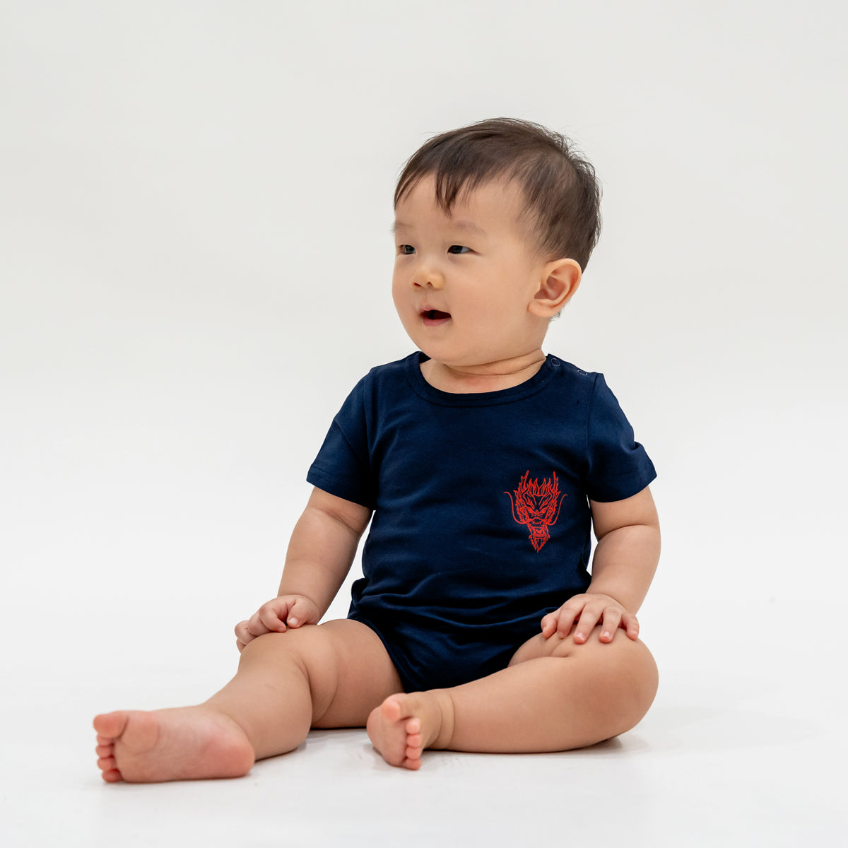 A baby boy in a navy blue romper with a red dragon print from Le Petit Society's Dragon Streetwear collection.