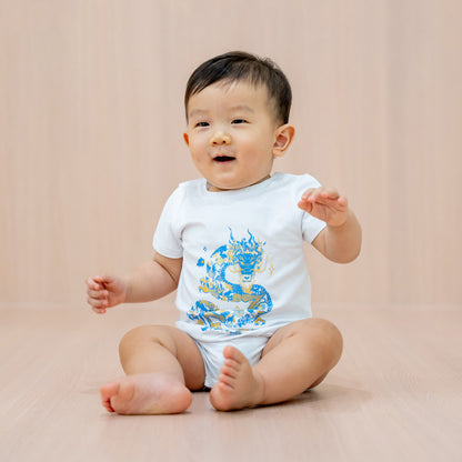 A baby boy in a white romper with a blue and gold dragon print from Le Petit Society's Dragon Streetwear collection.