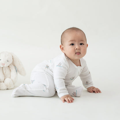 A baby wearing an organic zip sleepsuit in dragonfly print from Le Petit Society.