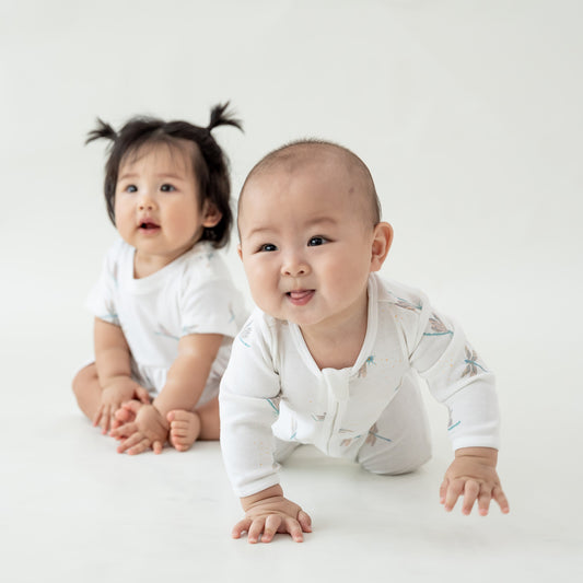 Two babies wearing pieces from Le Petit Society's organic baby line in dragonfly print.