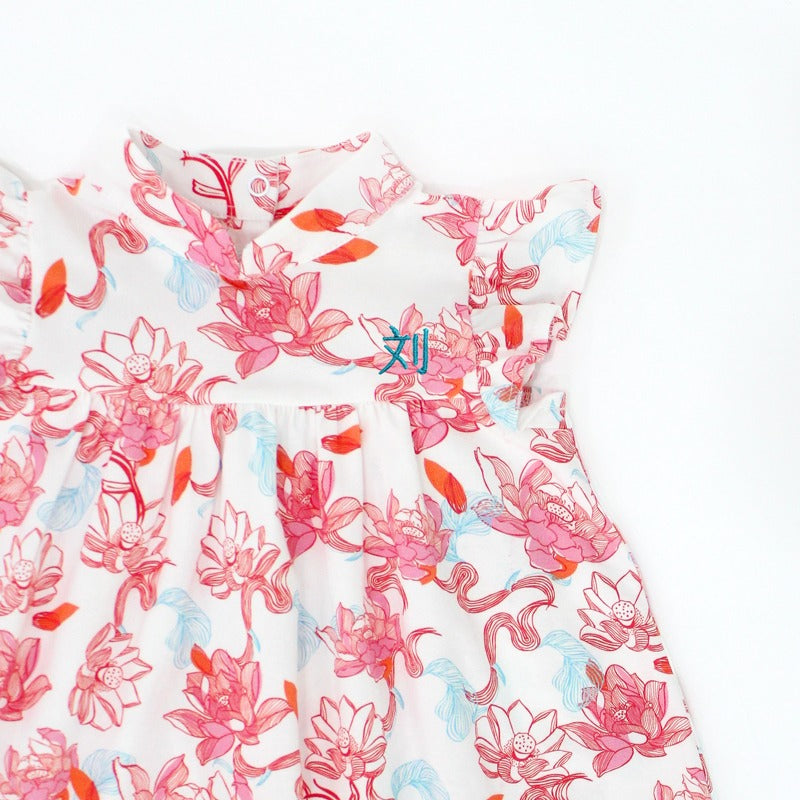 A close-up of the girls’ dress from the Le Petit Society x Sheila Sim CNY 2026 Lotus Collection. The soft mandarin neckline and flutter sleeves frame the gentle gathers at the bodice, while the coral and sky-blue lotus blooms flow seamlessly across the fa