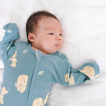 A newborn baby in a mint blue, organic zip sleepsuit in elephant print by Le Petit Society.