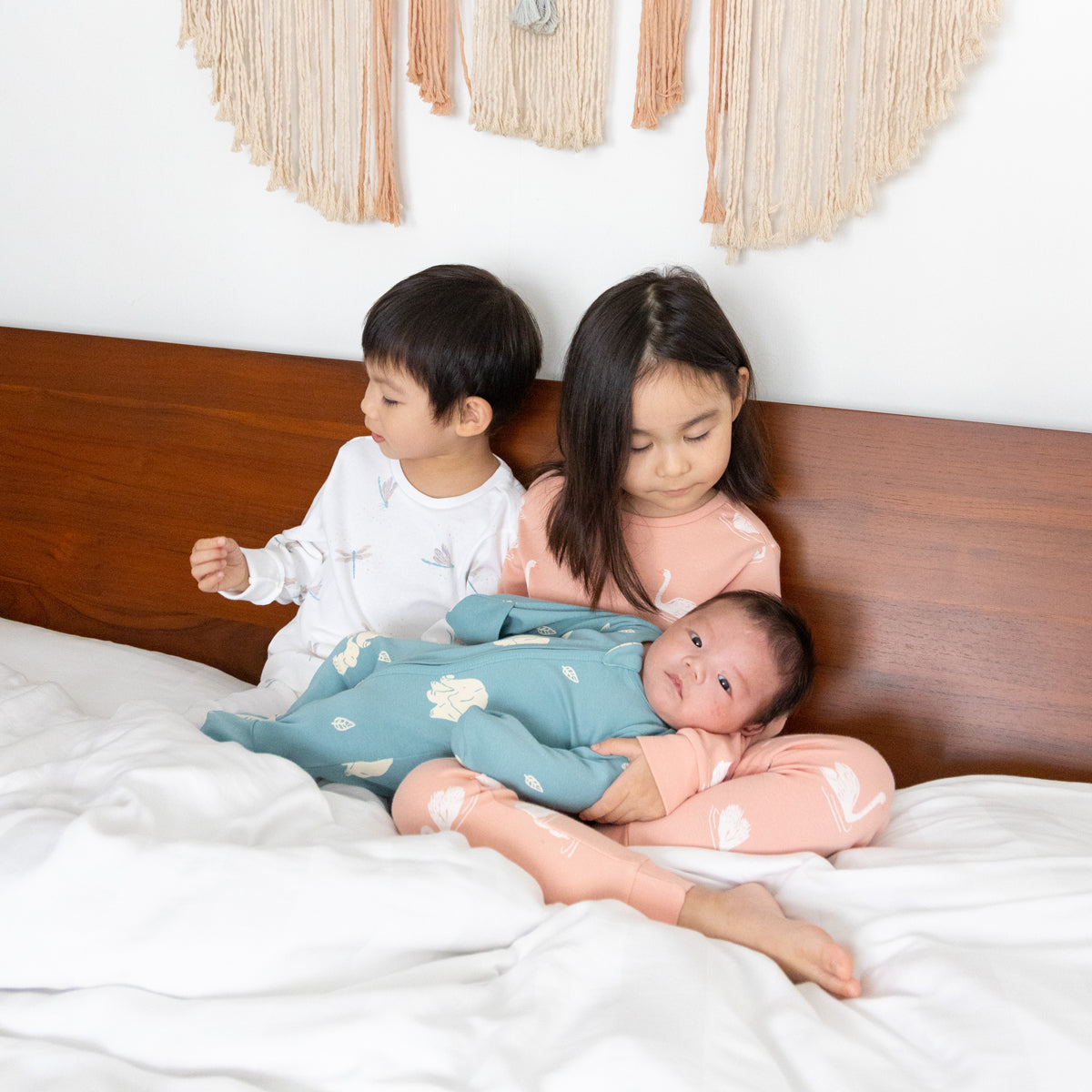 A baby, toddler and child all wearing sleepwear from Le Petit Society's organic line.