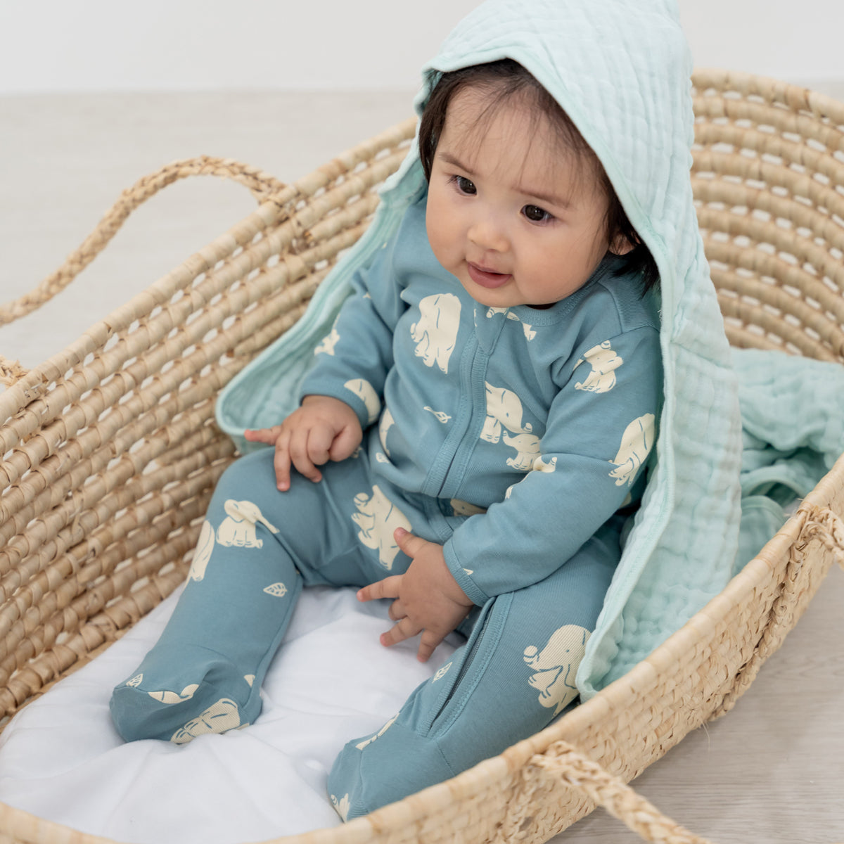 A baby girl wearing an organic zip sleepsuit in elephant print from Le Petit Society.