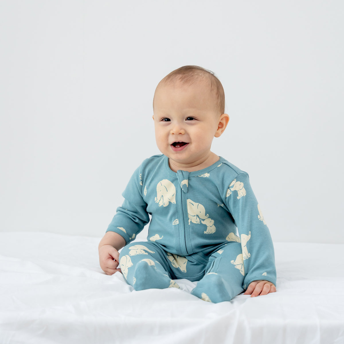 A baby wearing an organic zip sleepsuit in elephant print from Le Petit Society.