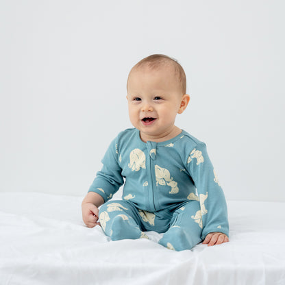 A baby wearing an organic zip sleepsuit in elephant print from Le Petit Society.