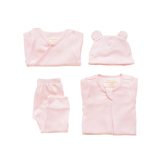 A baby organic essentials set in pink by Le Petit Society, consisting of a zip sleepsuit, kimono romper, leggings and bear hat.
