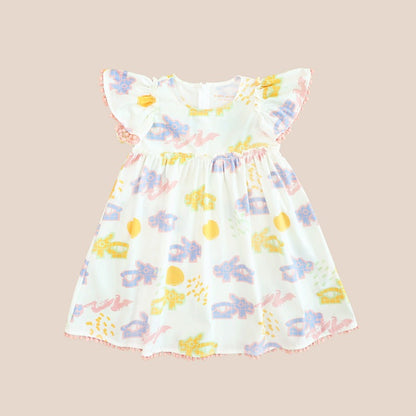 White girl’s flutter-sleeve dress from Le Petit Society with pink pompom trim and colorful dragon playground print and sun print in pastel blue, yellow, green, and pink.