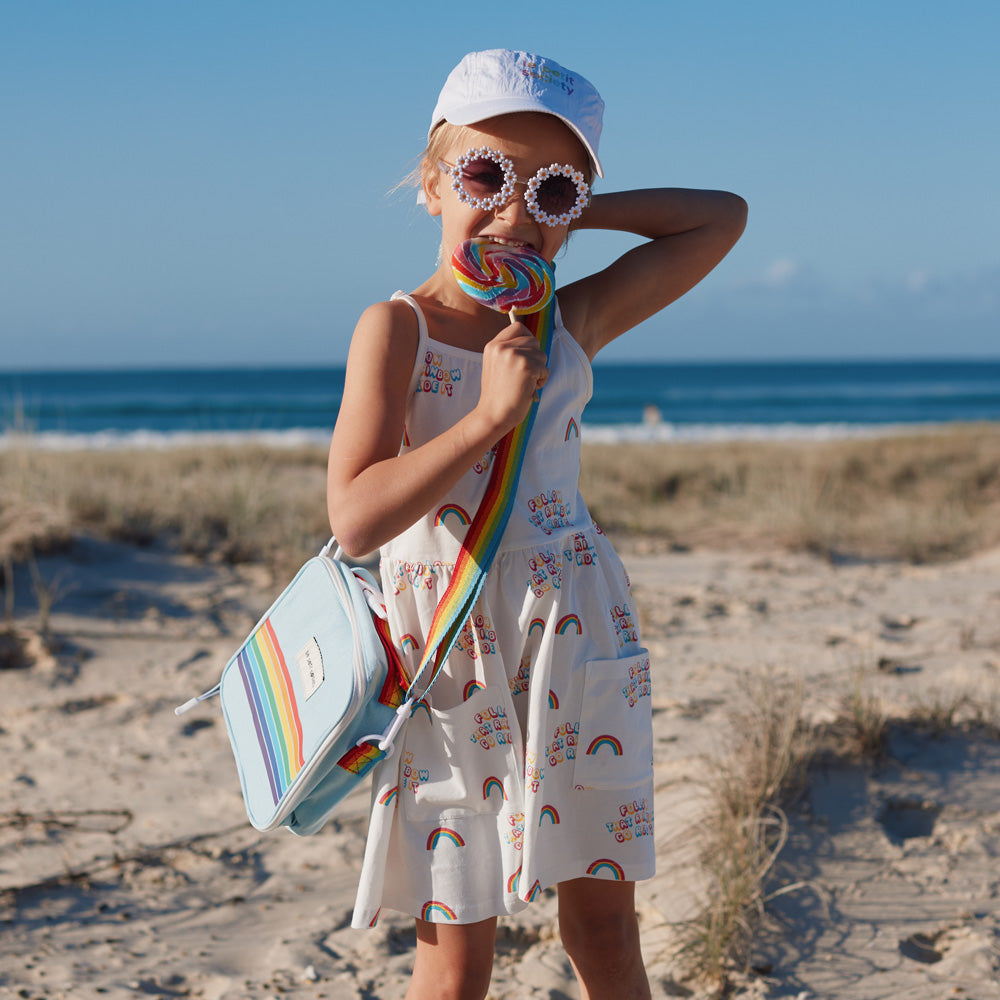 An elementary school girl with a dress and thermal lunch bag in rainbow print from Le Petit Society.