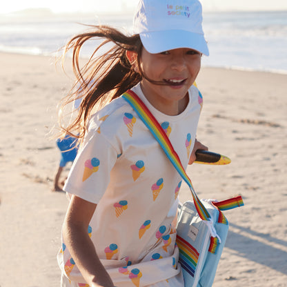 A happy girl carrying a thermal lunch bag with a rainbow print and strap from Le Petit Society.