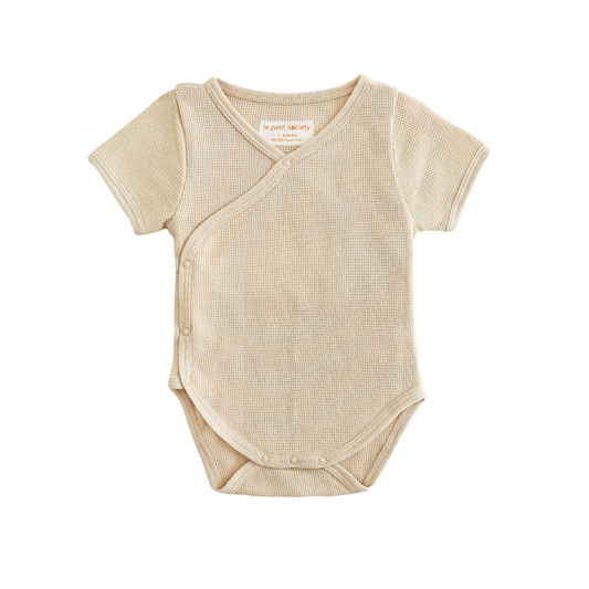 A baby organic kimono romper in beige by Le Petit Society.