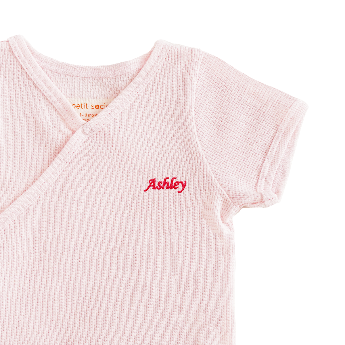 A close-up of a name embroidery personalisation on an organic baby kimono romper in pink by Le Petit Society.