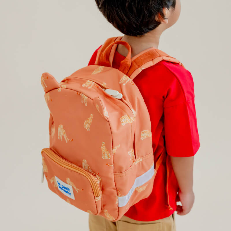 A little boy carrying an orange preschool bag with a leopard print.