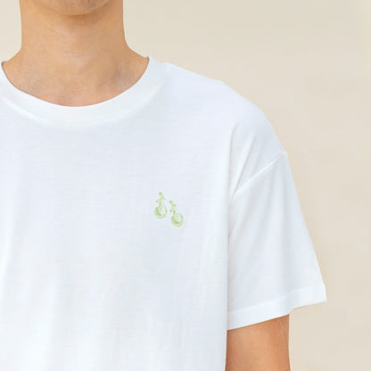 An adult male wearing a white tee with a small print of green pears from Le Petit Society.