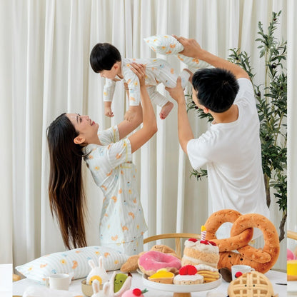 A family of three — mother, father, and baby boy — wearing coordinated breakfast print outfits from Le Petit Society, featuring illustrations of breakfast foods. 