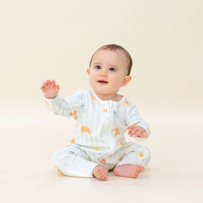 A baby boy wearing a bamboo sleepsuit from Le Petit Society, featuring a print of breakfast food and pastel green stripes.