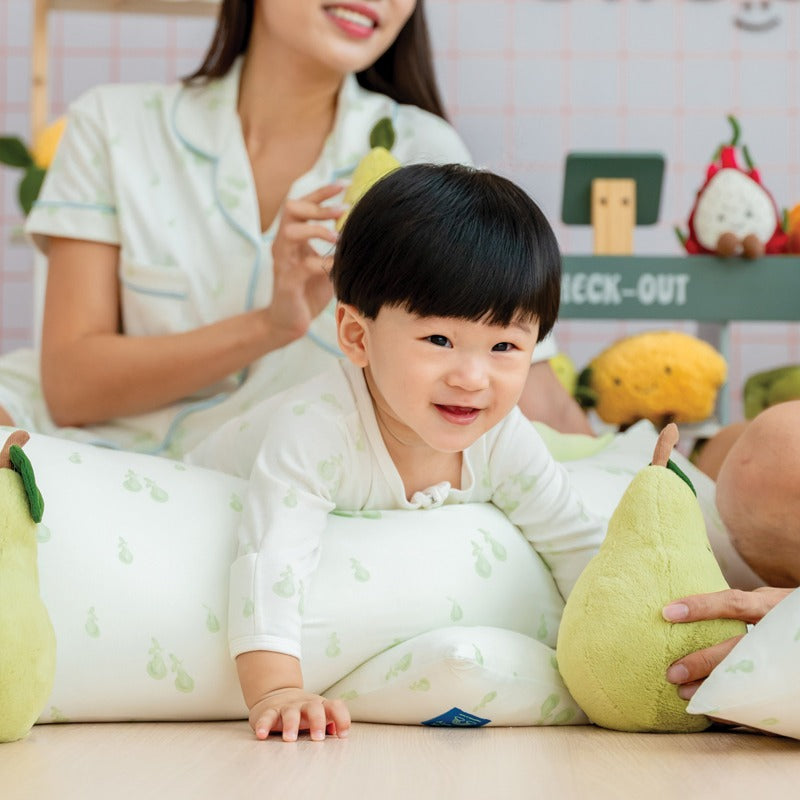 A baby boy in a sleepsuit with a pillow in a matching print of pears from Le Petit Society.